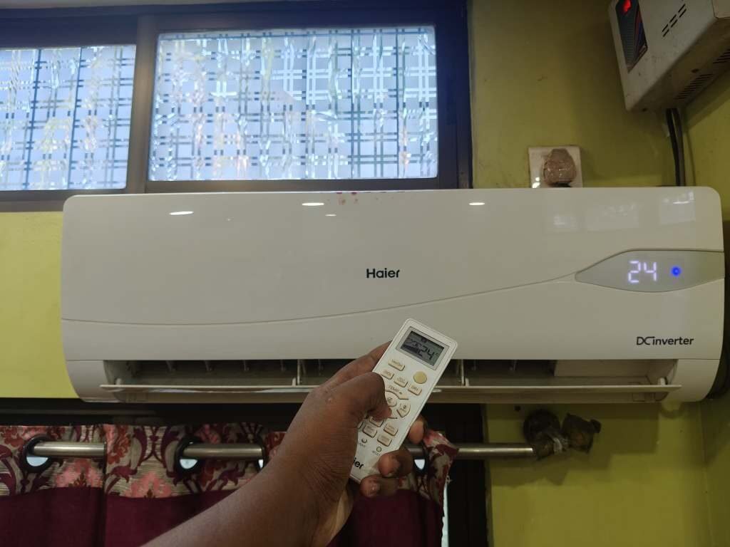 Haier split AC indoor unit mounted on a living room with BEE recommended AC temperature setting of 24°C displayed on a digital AC remote control