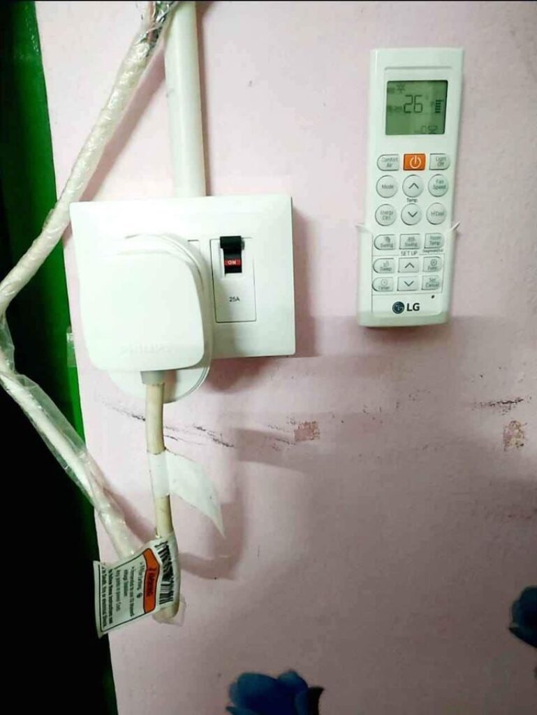 A white electrical outlet with a remote control attached, controlling an LG AC set at 26 degrees